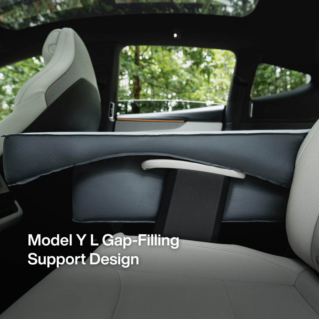 A dark gray car interior accessory shown installed between the front and rear seats of a Model Y or L, with white text reading 'Model Y L Gap-Filling Support Design' overlaid on the lower left. The seats are light gray, and trees are visible through the windows.